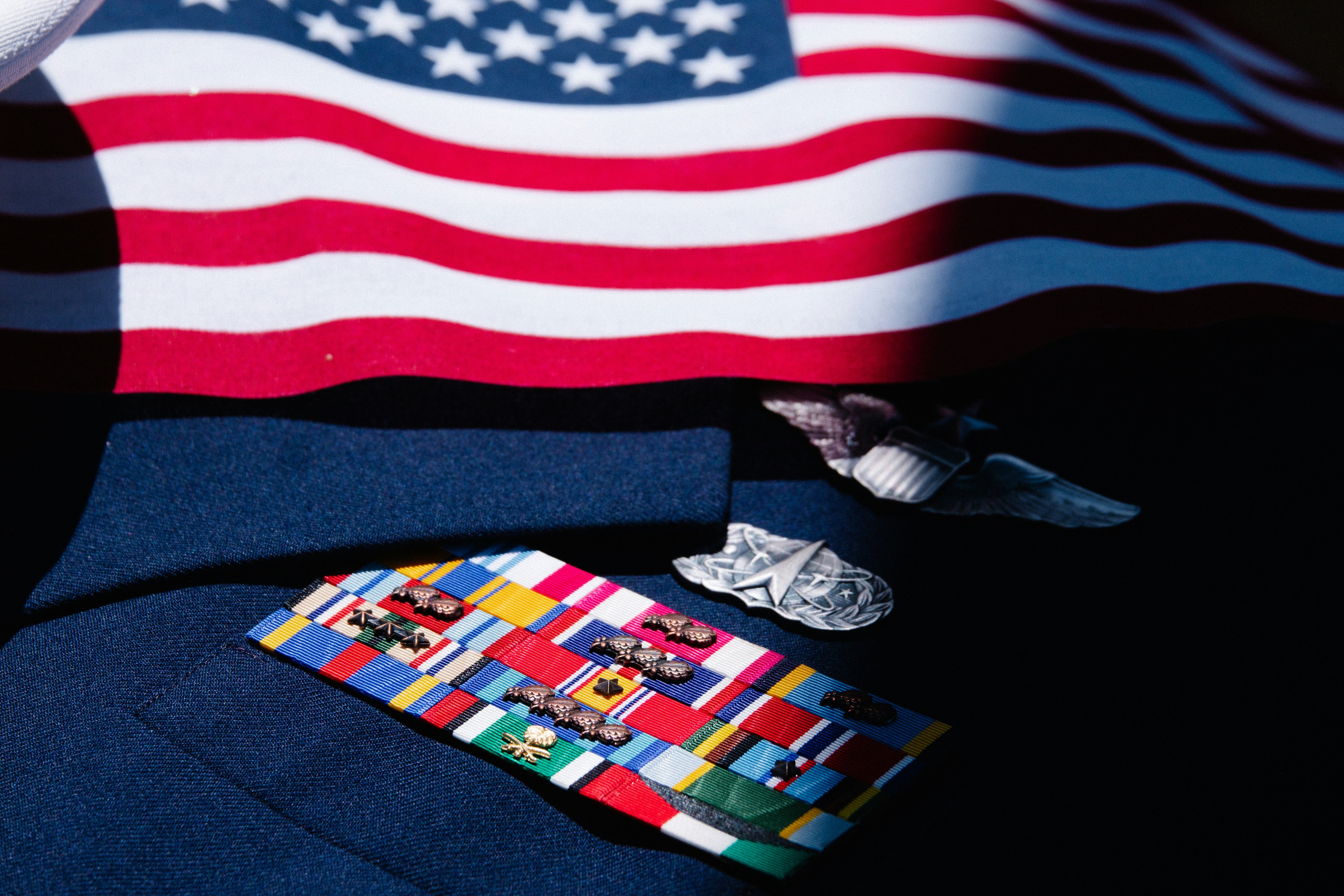 U.S. military dress uniform with service ribbons and medals beneath an American flag